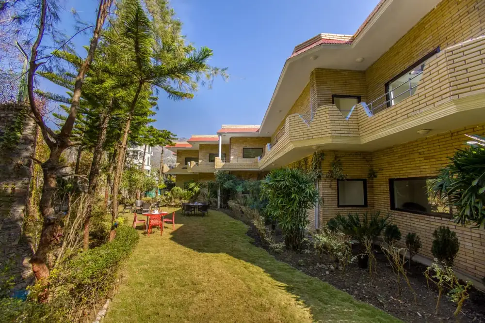 Lush green garden at Vaapi Comfort Inn surrounded by tall Himalayan trees